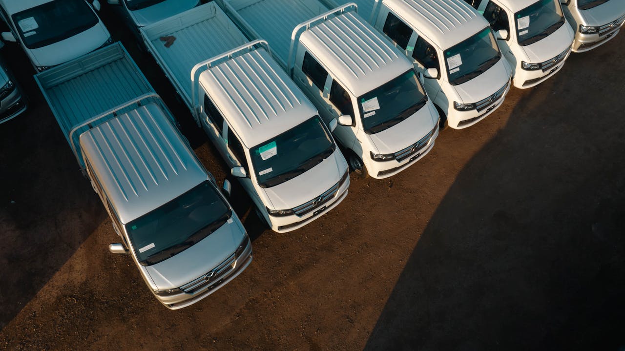 mission-img Aerial view of white pickup trucks aligned neatly in a parking lot. High contrast lighting.